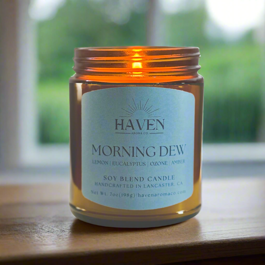 Candle in an amber jar labeled 'Morning Dew' by Haven with window background